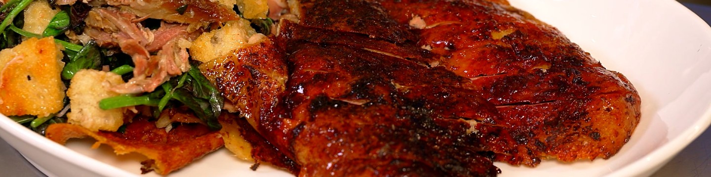 Close up of rotisserie duck salad with sliced duck on white plate.