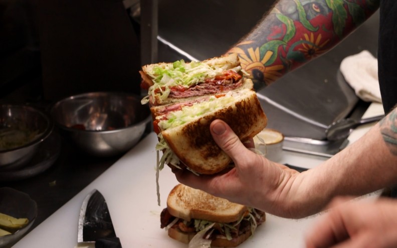 A hand holds a roast beef sandwich.