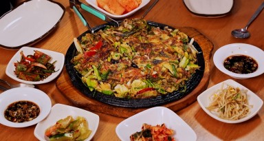A fried pancake-like dish on a plate surrounded by vegetables and sauces.