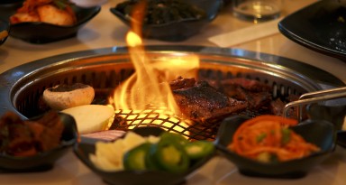A piece of meat being cooked by flame from a grill, located in the middle of a table.